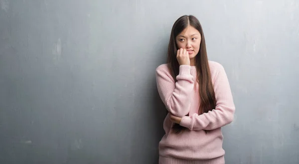 不安や緊張の爪を噛んで口の中に手を探している灰色の壁を越えて若い中国の女性 不安の問題 — ストック写真