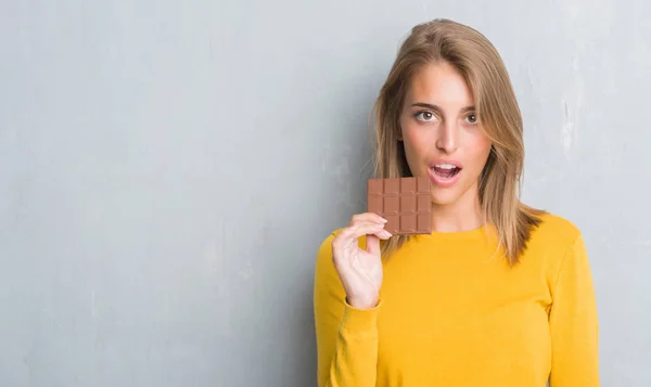 深刻な考えるスマートの顔に自信を持って式にチョコレート バーを食べてグランジ灰色の壁を越えて美しい若い女性 — ストック写真