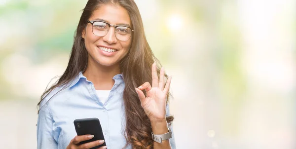 年轻美丽的阿拉伯妇女短信使用智能手机在孤立的背景做 符号与手指 优秀的符号 — 图库照片