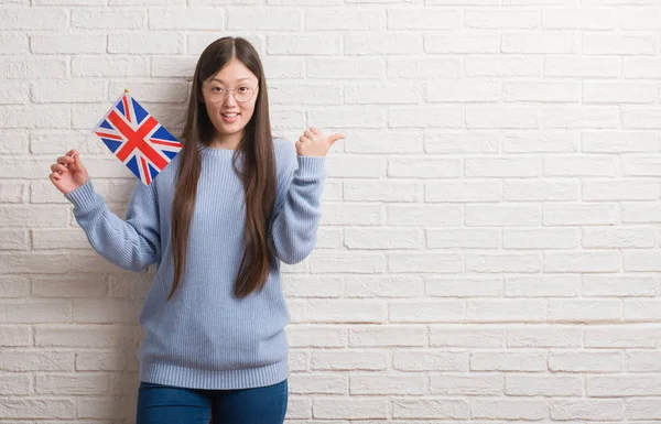 Joven Mujer China Sobre Pared Ladrillo Sosteniendo Bandera Inglaterra Señalando —  Fotos de Stock