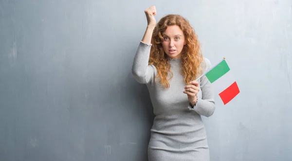 Молодая Рыжая Женщина Над Серой Гранж Стеной Держа Флаг Италии — стоковое фото