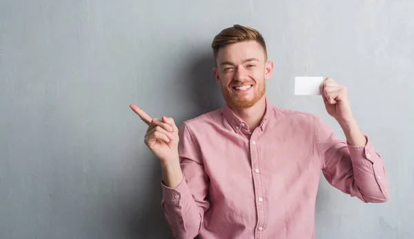 Joven Pelirrojo Sobre Pared Grunge Gris Sosteniendo Tarjeta Visita Blanco — Foto de Stock