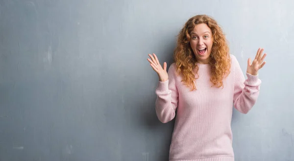 灰色のグランジ以上若い赤毛の女性は壁狂気を祝って びっくりの腕の成功のため興奮して叫んで調達と開いた目身に着けているピンクのセーターです 勝者の概念 — ストック写真