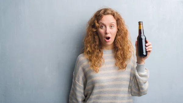 Молодая Рыжая Женщина Над Серой Гранж Стеной Держа Бутылку Пива — стоковое фото