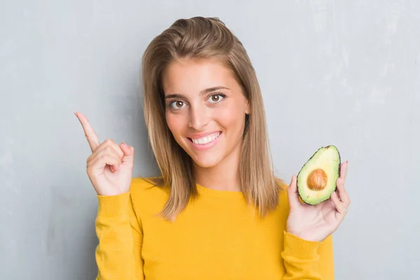 Beautiful Young Woman Grunge Grey Wall Eating Avocado Surprised Idea — Stock Photo, Image