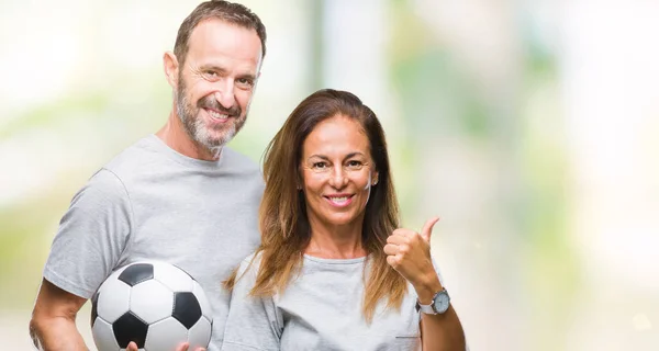 指していると幸せそうな顔を笑顔で側まで親指で示す分離の背景にサッカー サッカー ボールを保持している中年ヒスパニック系カップル — ストック写真
