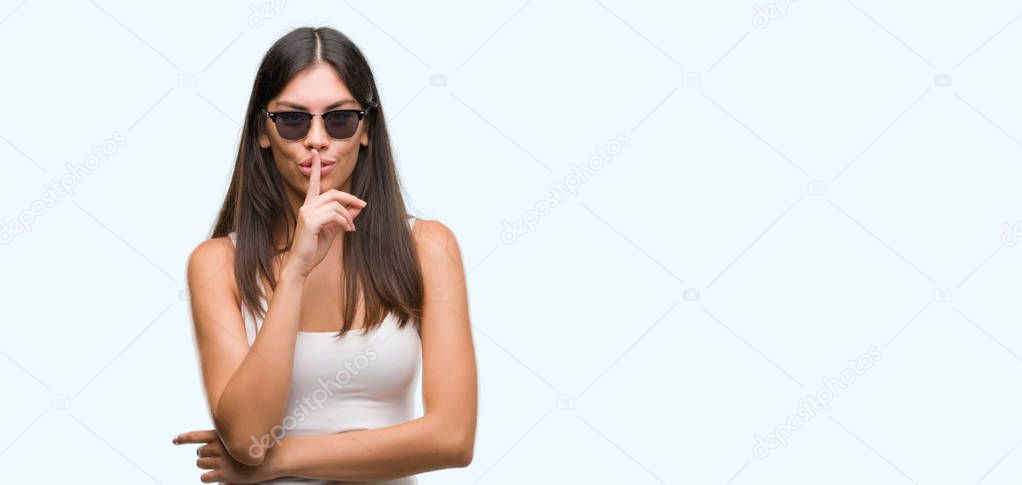 Young beautiful hispanic wearing sunglasses asking to be quiet with finger on lips. Silence and secret concept.
