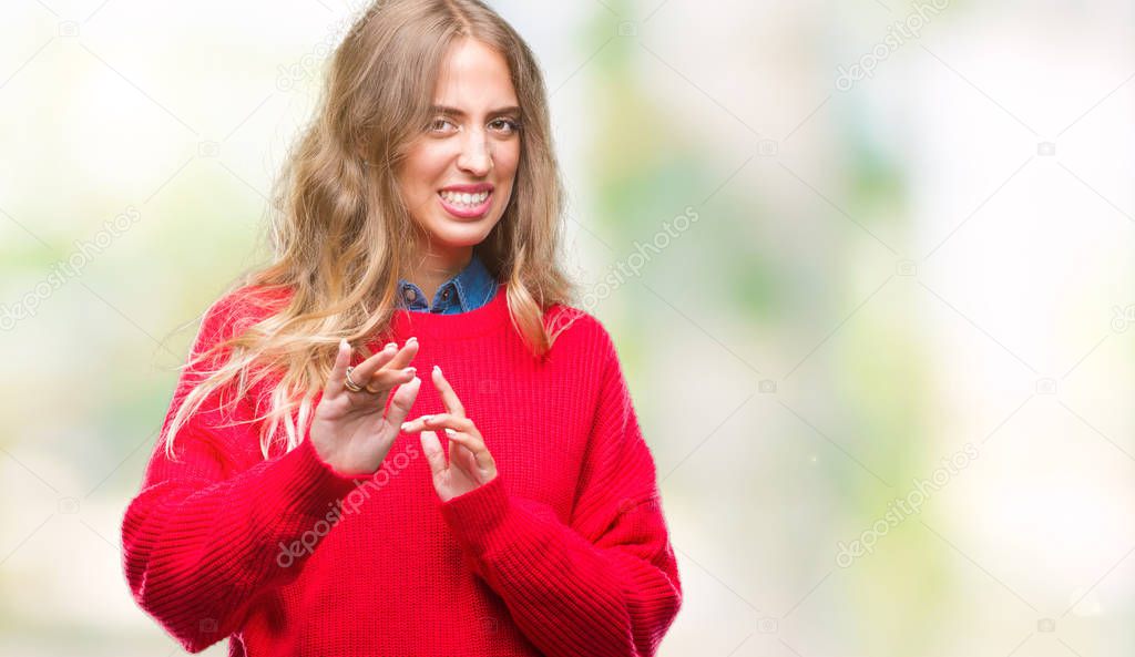 Beautiful young blonde woman wearing winter sweater over isolated background disgusted expression, displeased and fearful doing disgust face because aversion reaction. With hands raised. Annoying concept.