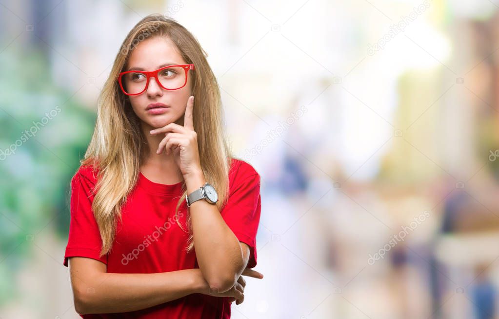 Young beautiful blonde woman wearing glasses over isolated background with hand on chin thinking about question, pensive expression. Smiling with thoughtful face. Doubt concept.