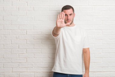 Genç beyaz adam eliyle yapım çerçeve ve parmakları ile mutlu yüz gülümseyen beyaz tuğla duvarın üzerinden ayakta. Yaratıcılık ve Fotoğrafçılık kavramı.