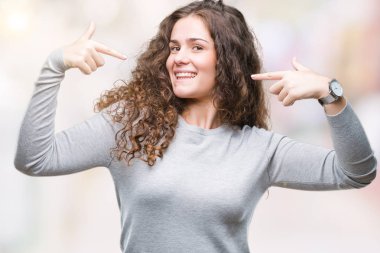 Yüzünde gülümseme ile kendinden emin görünüyorsun, kendini gururlu ve mutlu parmakları ile işaret izole arka plan üzerinde bir kazak giyen güzel esmer kıvırcık saçlı Genç kız.