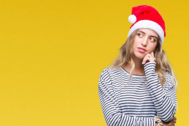 Çene düşünme hakkında soru, dalgın ifade üzerine el ile izole arka plan üzerinde Noel şapka giyen güzel genç sarışın kadın. Düşünceli yüzüyle gülümsüyor. Şüphe kavramı.