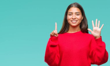 Genç güzel Arap kadın giyiyor kış kazak gösterilen ve parmakları ile işaret izole arka plan üzerinde kendinden emin ve mutlu gülümseyerek süre 6 numara.