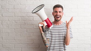 Genç yetişkin adam tutarak büyük gülümseme ile çığlık zaferini kutluyor çok mutlu ve heyecanlı, kazanan ifade megafon ve ellerini kaldırdı