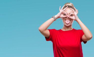 Dilini, parmaklarının arasından baktığını yapışmasını dürbün gibi ok jest yapıyor izole arka plan üzerinde gözlüklü sarışın genç kadın. Deli ifade.