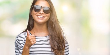 Genç güzel Arap kadın hareketi el ile mutlu yaşasın yapıyor izole arka plan üzerinde güneş gözlüğü takıyor. Kameraya bakarak başarı gösteren ile ifade onaylama.