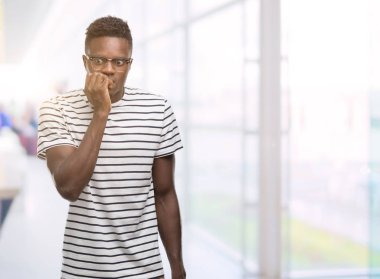 Gözlük ve stresli ve gergin elle çivi ısırma ağzına bakarak lacivert t-shirt giyen genç Afro-Amerikan adam. Anksiyete sorunu.