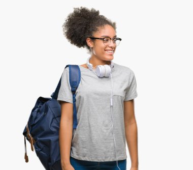 Üzerinde kulaklık ve sırt çantası giyen genç afro Amerikan öğrenci kadın arka plan uzak tarafına gülümseme ile yüzünde, doğal ifade arıyorum izole. Kendine güvenen gülüyor.