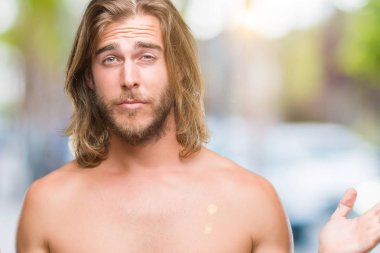 Genç yakışıklı gömleksiz adam uzun saçlı seksi vücut üzerinde gösterilen arka plan clueless ve şaşkın bir ifadeyle kollar ve eller kaldırdı izole. Şüphe kavramı.