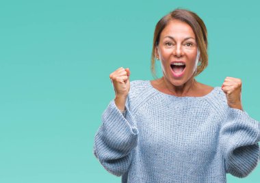 İzole arka plan üzerinde kutluyor kış kazak giyen orta yaş üst düzey İspanyol kadın şaşırttı ve başarı için kaldırdı kollarını açarak hayret ve gözleri açık. Kazanan kavramı.