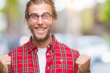 Uzun saçlı izole arka plan üzerinde kutluyor gözlük takan yakışıklı delikanlı şaşırttı ve başarı için kaldırdı kollarını açarak hayret ve gözleri açık. Kazanan kavramı.