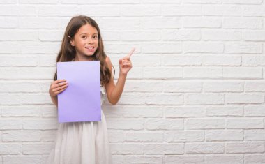 Beyaz tuğla duvar pembe kağıt levha çok mutlu el ve parmak ile tarafına işaret tutan genç İspanyol çocuk