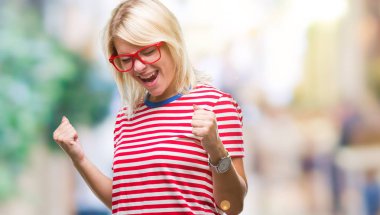 Genç güzel sarışın kadın üzerinde gözlük gülümseyen ve başarı için çığlık arka plan çok mutlu ve heyecanlı kaldırdı, silah ile kazanan jest yapıyor izole. Kutlama kavramı.