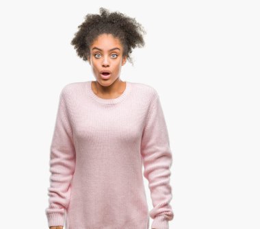 Korkuyor ve şok sürpriz ifade, korku ve heyecan yüz ile izole arka plan üzerinde kış kazak giyen genç afro Amerikan kadın.