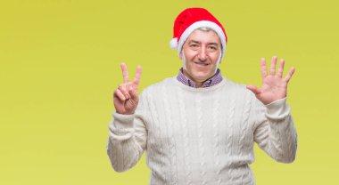 Üst düzey yakışıklı Noel şapka üzerinde gösterilen arka plan izole ve parmakları ile işaret kendinden emin ve mutlu gülümseyerek süre yedi numara.