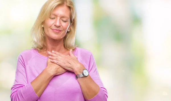 Middle age blonde woman over isolated background smiling with hands on chest with closed eyes and grateful gesture on face. Health concept.