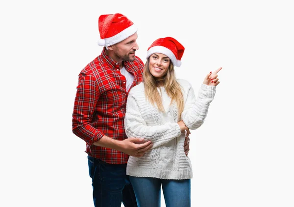 カメラを見ている側の手と指で指すの顔に大きな笑みを浮かべて隔離された背景にクリスマスの帽子をかぶって恋若いカップル — ストック写真