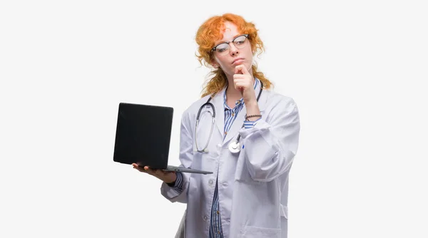 Νέοι Κοκκινομάλλα Γυναίκα Γιατρός Κρατώντας Υπολογιστή Laptop Σοβαρό Πρόσωπο Σκεφτόμαστε — Φωτογραφία Αρχείου