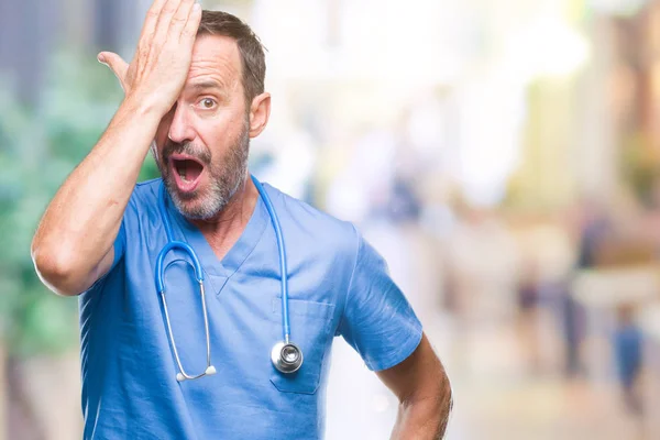 Middle age hoary senior doctor man wearing medical uniform over isolated background surprised with hand on head for mistake, remember error. Forgot, bad memory concept.