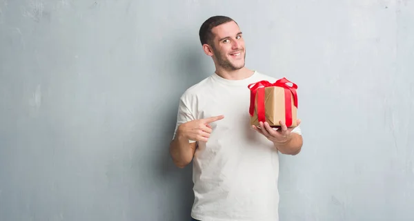 Joven Caucásico Hombre Sobre Gris Grunge Pared Sosteniendo Regalo Muy —  Fotos de Stock