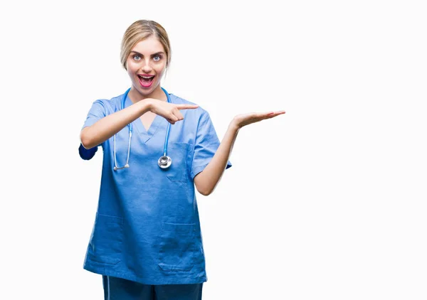 驚くし 手とを提示 指で指している間カメラに笑顔孤立の背景に美しい金髪女医外科医看護師女性 — ストック写真