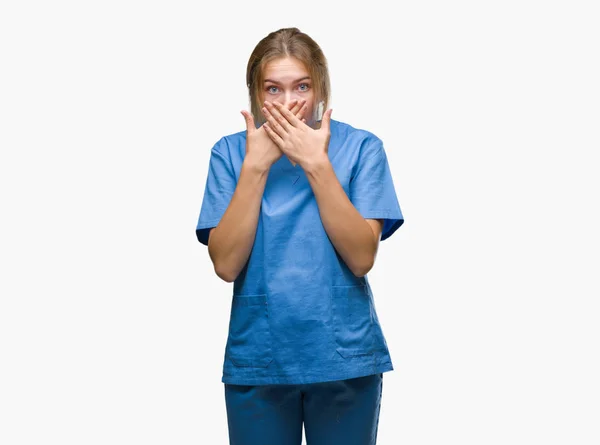 ミスのため手で口を覆っているショックを受けて孤立の背景の上の外科医の制服を着て若い白人の看護師の女性 秘密の概念 — ストック写真
