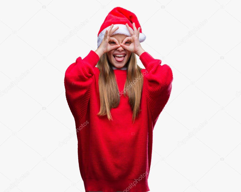 Young beautiful girl wearing christmas hat over isolated background doing ok gesture like binoculars sticking tongue out, eyes looking through fingers. Crazy expression.