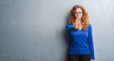 Elin avuç durağı şarkı yapıyor gri grunge duvarın üzerinden genç Kızıl saçlı kadın. Negatif ve ciddi bir jest yüz ifadesiyle uyarı.