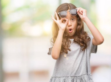 Esmer Latin kız ok jest sürpriz yüz, göz parmaklarının arasından seyir şok yapıyor güneş gözlüğü takıyor. İmansız ifade.