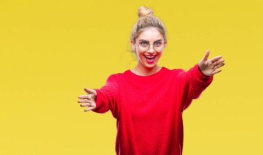 Sarılmak için kollarını açarak gülümseyerek kameraya bakarak izole arka plan üzerinde kırmızı kazak ve gözlük giyen genç güzel sarışın kadın. Neşeli ifade kucaklayan mutluluk.