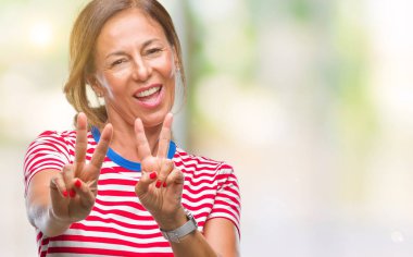 Orta yaş üst düzey İspanyol kadın parmaklarını zafer işareti yaparken gösterilen kamera seyir gülümseyen izole arka plan yüzünden. İki numaralı.