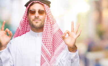 Genç yakışıklı adam giyen keffiyeh izole arka plan üzerinde dinlenmek ve gülümseyen gözlerle parmak ile meditasyon jest yapıyor kapalı. Yoga kavramı.