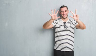 Beyaz delikanlı gösterilen ve parmakları ile işaret gri grunge duvarın üzerinden sekiz kendinden emin ve mutlu gülümseyerek iken numara.