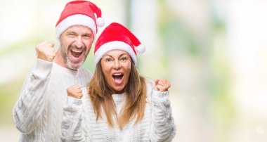 Orta yaş İspanyol çift izole arka plan kutlama üzerinde Noel şapka şaşırttı ve başarı için kaldırdı kollarını açarak hayret ve gözleri açık. Kazanan kavramı.