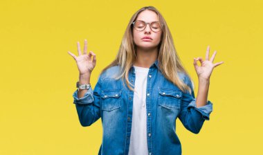 Genç güzel sarışın kadın gözlük izole arka plan üzerinde dinlenmek ve gülümseyen gözlerle kapalı parmak jestle meditasyon yapıyor. Yoga kavramı.