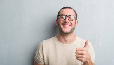 Ok işareti, başparmak ile parmak, mükemmel işareti yapıyor kocaman bir gülümseme ile mutlu gri grunge duvarın üzerinden beyaz delikanlı