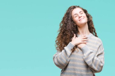 Güzel esmer kıvırcık saçlı Genç kız üzerinde gülümseyen izole arka plan ile kış kazak giyen kapalı gözler ve yüzünde minnettar jest ile göğüs üzerinde eller. Sağlık kavramı.
