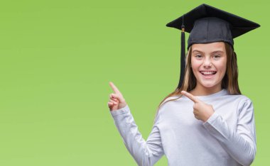 Genç güzel kız gülümseyerek ve iki elleri ve parmakları ile tarafına işaret kamera bakarak izole arka plan üzerinde yüksek lisans şapkası.