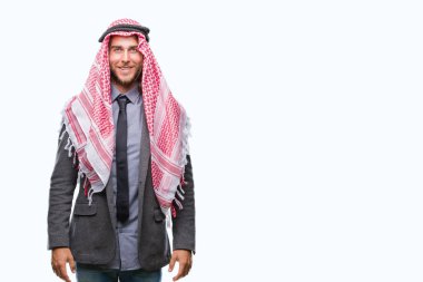 Genç yakışıklı Arap adam uzun saçlı yüzünde mutlu ve güzel bir gülümseme ile izole arka plan üzerinde keffiyeh giyiyor. Şanslı kişi.