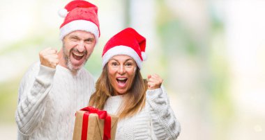 Orta yaş İspanyol çift gurur çığlık ve zafer ve başarı çok heyecanlı, duygu tezahürat kutluyor izole arka plan üzerinde giyen Noel şapka ve holding Hediyelik